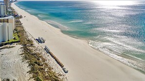 Une plage avec un rivage sablonneux, un océan d’un bleu limpide et des bâtiments qui bordent la côte.