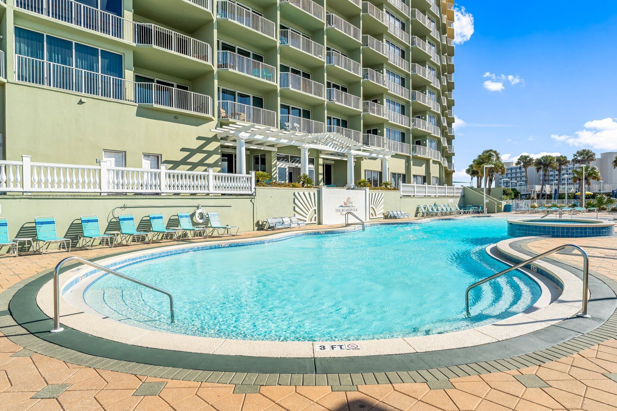 Un hotel con una piscina grande, varios balcones y una zona cubierta con sillones de descanso.