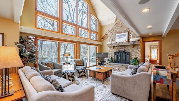 A spacious living room with high ceilings, large windows, and a stone fireplace. - Dog Friendly Lakefront Home w/ Dock & Hot Tub (MCHENRY)
