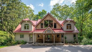 A large, two-story house with a red roof, a stone facade, and a porch with a bench. - Dog Friendly Lakefront Home w/ Dock & Hot Tub (MCHENRY)