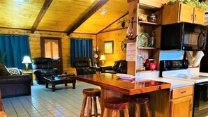 A cozy wooden interior with a kitchen area, wooden stools, a dining table, and a sofa. - Beautiful 3 Bedroom, 2 Bath. Private Backyard. 321 Bayshore Dr. (Port Mansfield)