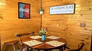 A wooden interior with a round table and chairs, a Coca-Cola poster, and a sign reading "THE GATHERING PLACE". - Beautiful 3 Bedroom, 2 Bath. Private Backyard. 321 Bayshore Dr. (Port Mansfield)