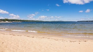 A beach with clear water, distant hills, and a clear sky.