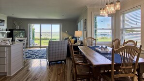 A dining area with a wooden table and chairs, a blue patterned rug, and a view of a green landscape through large windows.
