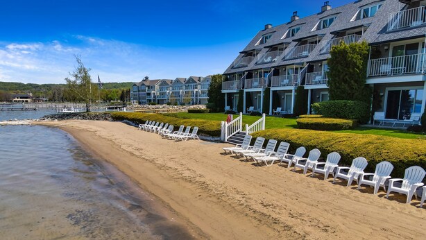 A beachfront hotel with multiple balconies, a clear view of the water, and a row of white beach chairs along the shore.