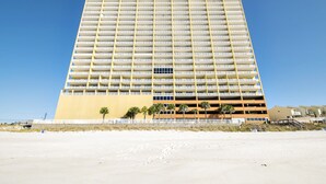 A high-rise hotel with multiple floors, a flat roof, and a sandy beach in the foreground.