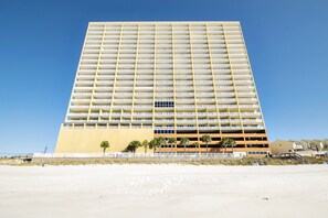 Un hotel de gran altura con varios pisos, techo plano y una playa de arena al frente.