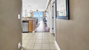 A hallway leading to a kitchen with a view to the outside.