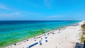 A beach with clear turquoise water, white sand, and numerous umbrellas.