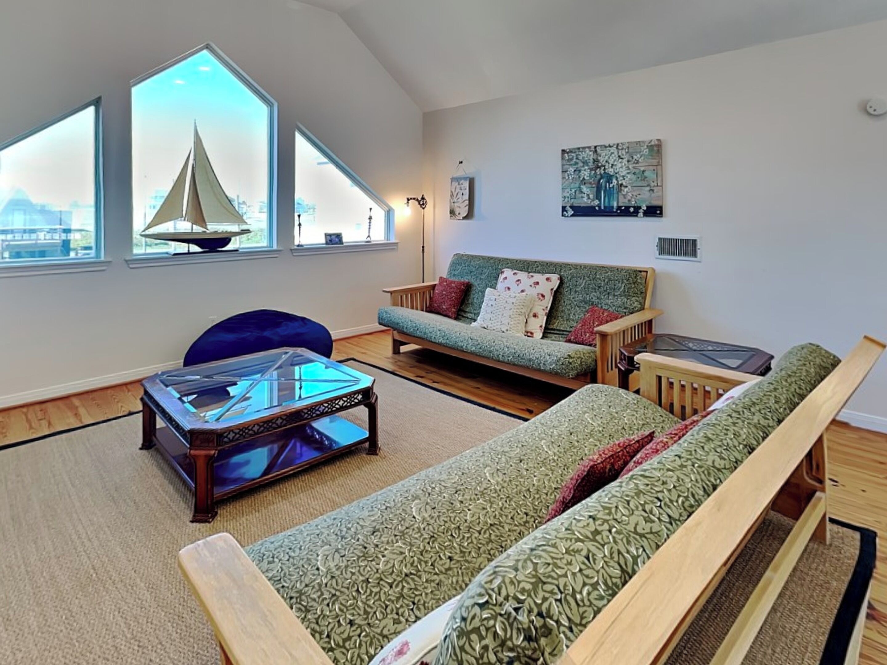 A living room with a sofa, a coffee table, and a chair. There are large windows with a sailboat model and a city view.