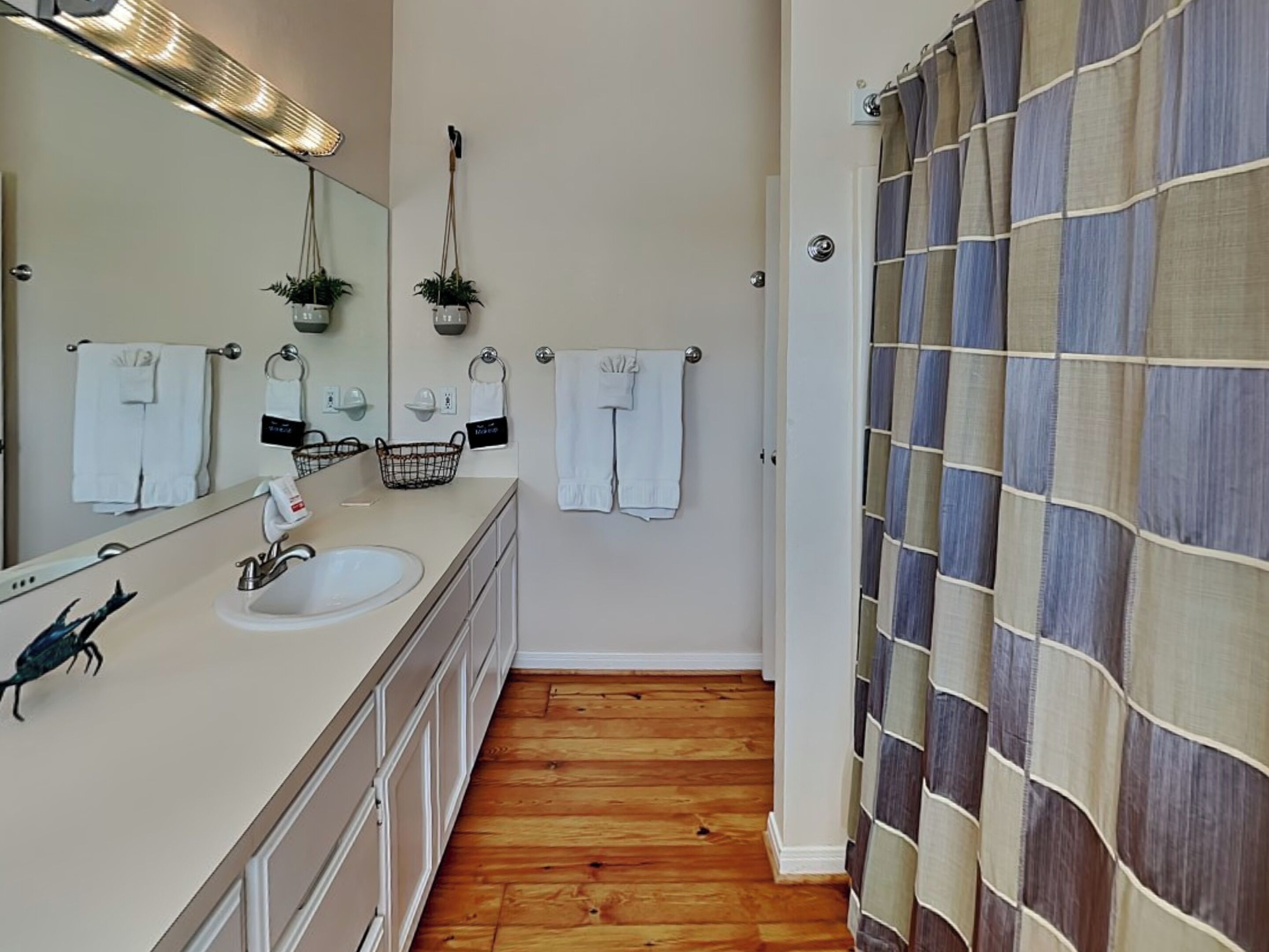A bathroom with a wooden floor, a sink with a mirror, and a shower curtain with a plaid pattern.