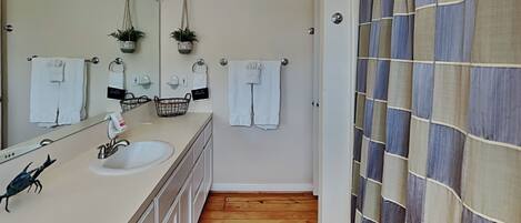 A bathroom with a wooden floor, a sink with a mirror, and a shower curtain with a plaid pattern.
