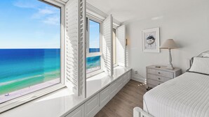 A bedroom with a large window overlooking a beach, a bedside table with a lamp, and a framed picture on the wall. - Beachfront Condo w/ GOLF CART, Furnished Balcony, Gulf View, Pool, Beach Tram (Miramar Beach)
