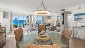 A spacious living room with a glass dining table, wicker chairs, and a view of the ocean. - Beachfront Condo w/ GOLF CART, Furnished Balcony, Gulf View, Pool, Beach Tram (Miramar Beach)