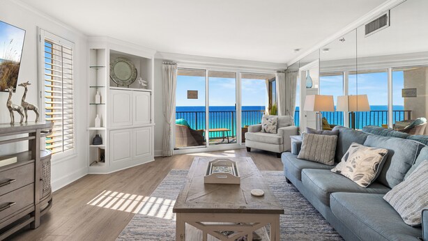 A spacious living room with a large window overlooking the ocean, a sofa, a coffee table, and a sideboard. - Beachfront Condo w/ GOLF CART, Furnished Balcony, Gulf View, Pool, Beach Tram (Miramar Beach)