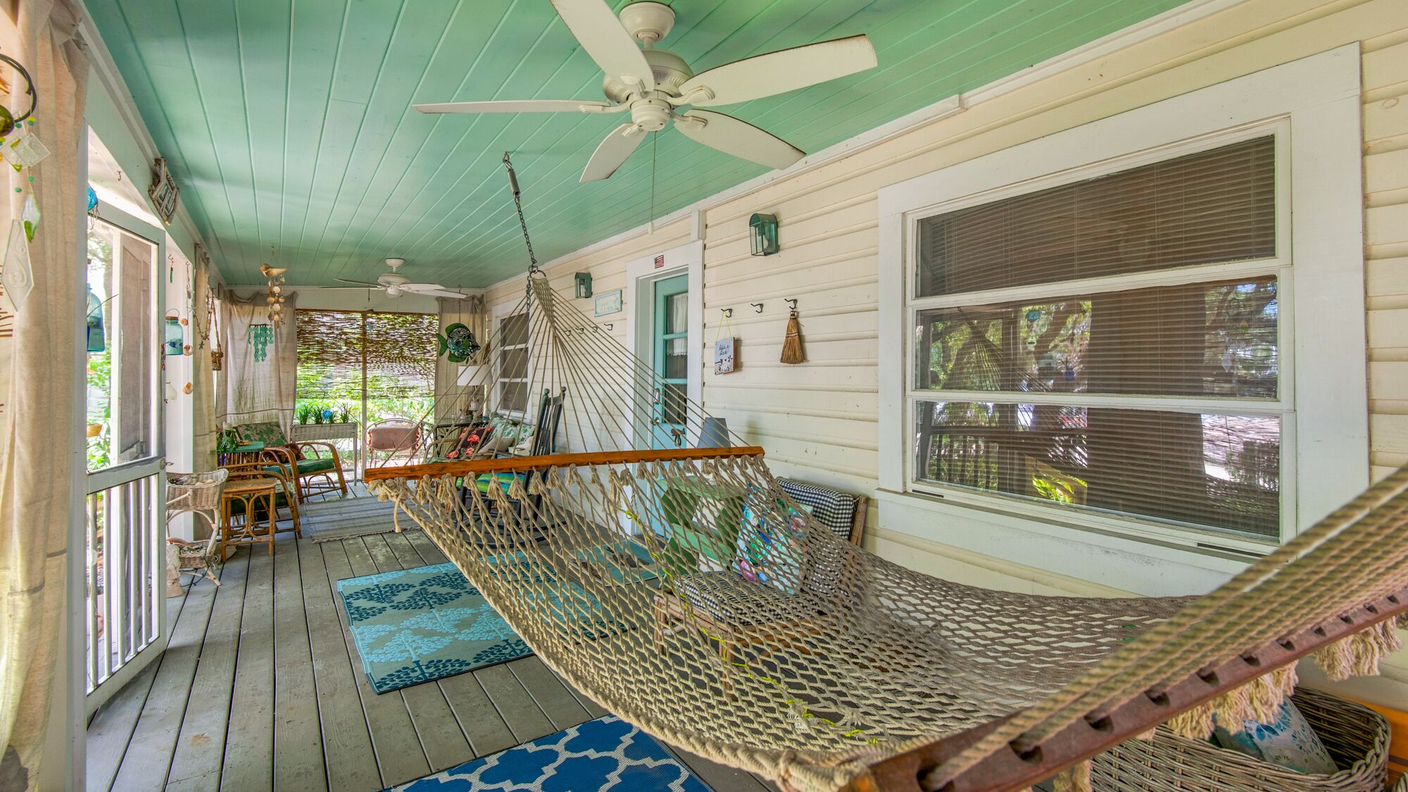 A porch with a hammock, wooden deck, and a ceiling fan.