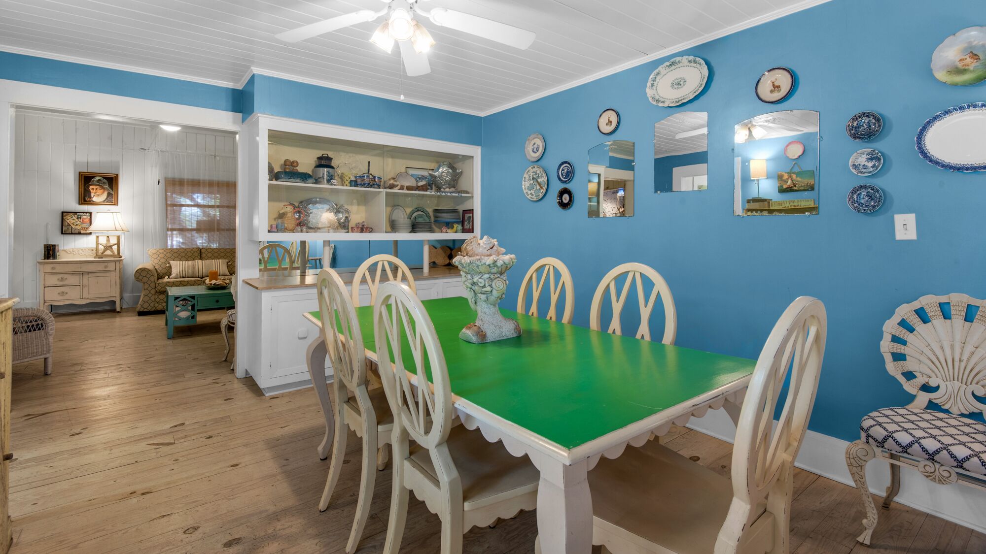 Een eethoek met een groene tafel en witte stoelen, omringd door blauwe wanden en diverse decoratieve borden.