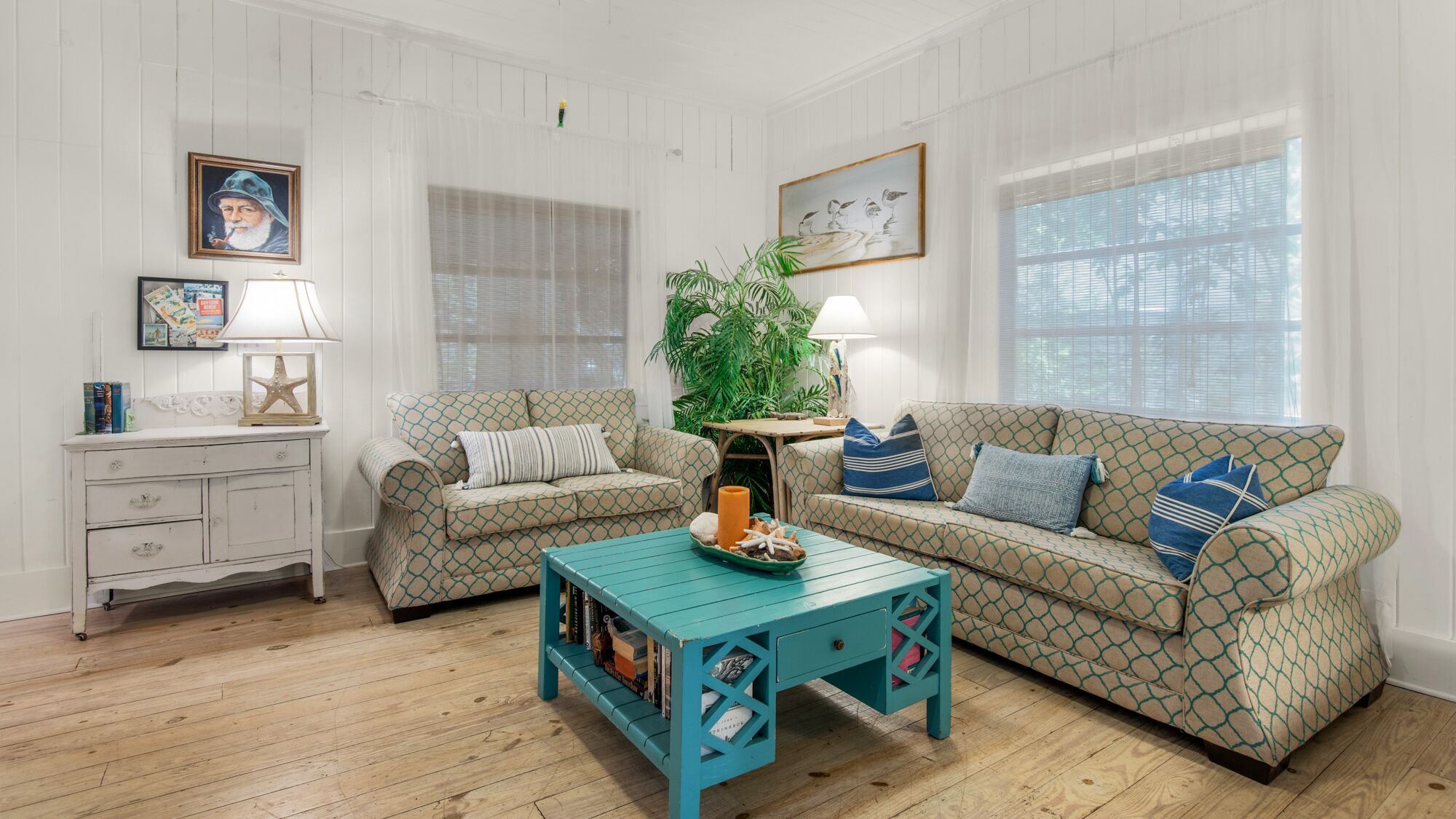Un salon chaleureux avec deux canapés à motifs, une table basse de couleur turquoise et une commode blanche.