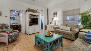 A cozy living room with a television, a patterned sofa, a small table with books, and a decorative fish tank. - Close to Beach & Seaside, Vintage Cottage + Free Attraction Tickets! (Santa Rosa Beach)