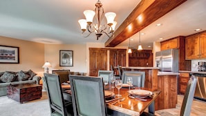 Un comedor con una mesa de madera, sillas y una araña. Hay una cocina con gabinetes de madera y electrodomésticos de acero inoxidable.