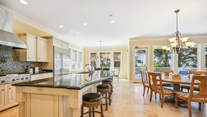 A spacious kitchen with a central island, stainless steel appliances, and a dining area with wooden chairs and a chandelier. - 18 Sand Dollar, Oceanfront, Pool, Free Golf, Elevator, Great Views (Hilton Head Island)