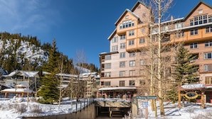 A multi-story hotel with a ski lift entrance, surrounded by snow-covered trees and a clear sky.
