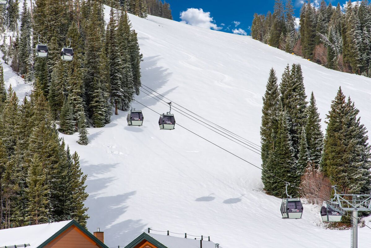A ski lift with cabins descending a snowy slope, surrounded by evergreen trees.