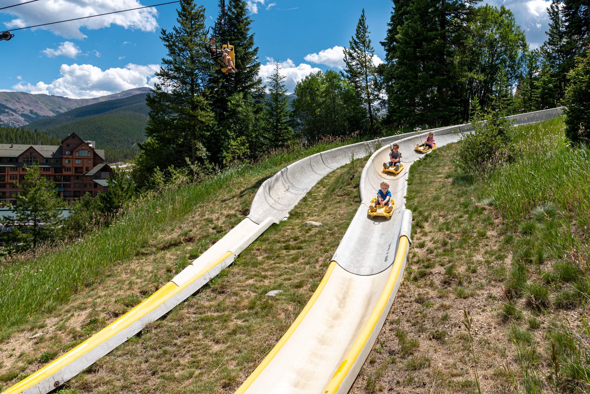 A ski lift with passengers in yellow chairs descending a steep, grassy slope.