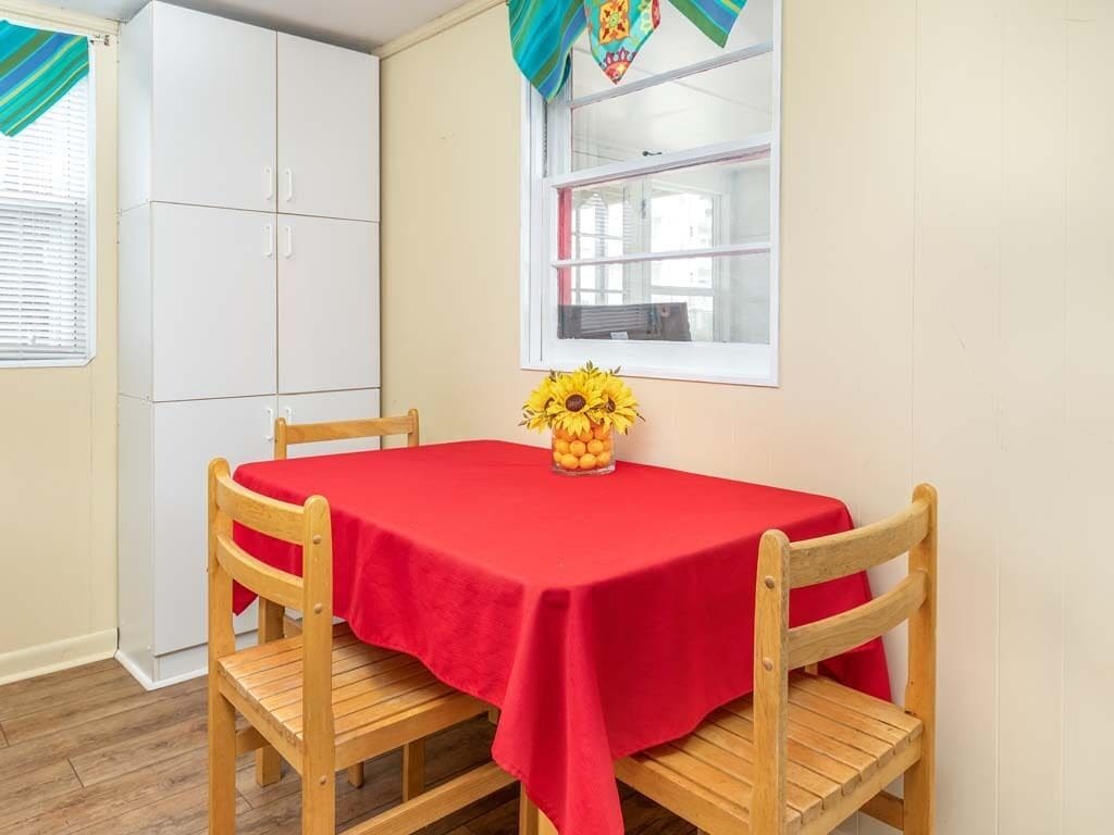 A room with a red table, two wooden chairs, a window with blinds, and a white wardrobe.