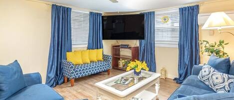 A living room with a sofa, a coffee table, a ceiling fan, and a television.