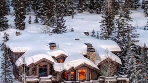 A log cabin with a snow-covered roof, surrounded by snow-laden trees.