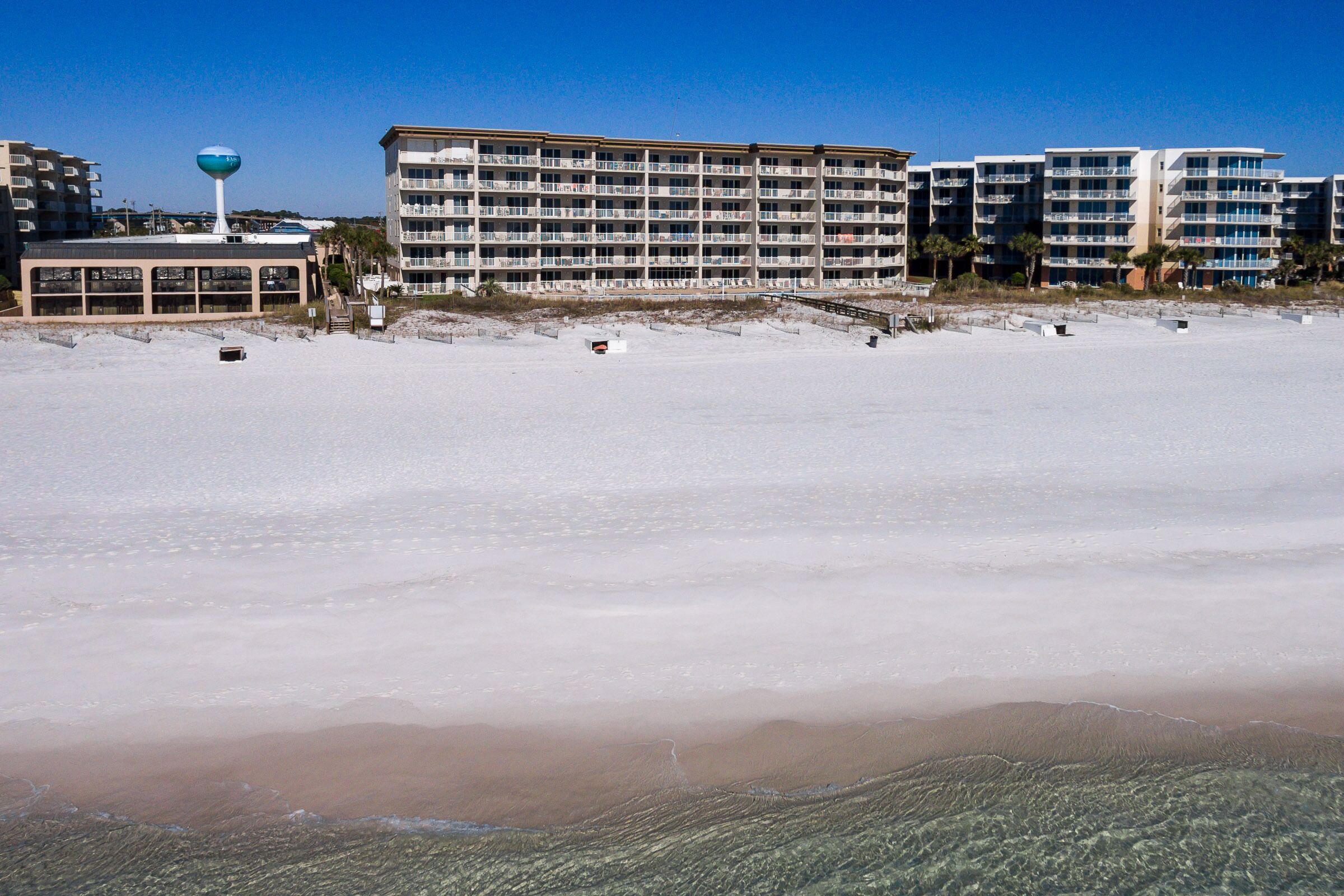 Un hotel frente a la playa con varios balcones, un tanque de agua y una playa de arena.