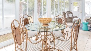 A glass-top table with wicker chairs and a woven basket in a sunroom with large windows and a ceiling fan. - Driftaway | Ocean Views, Dual Sun Rooms (Tybee Island)