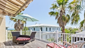 A wooden deck with outdoor furniture, a white railing, and a view of a white building. - Driftaway | Ocean Views, Dual Sun Rooms (Tybee Island)