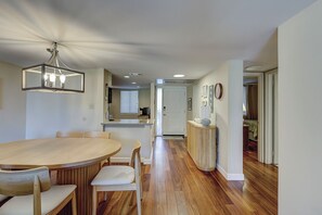 A modern kitchen with a wooden dining table and chairs, a pendant light, and a hallway leading to a bedroom.