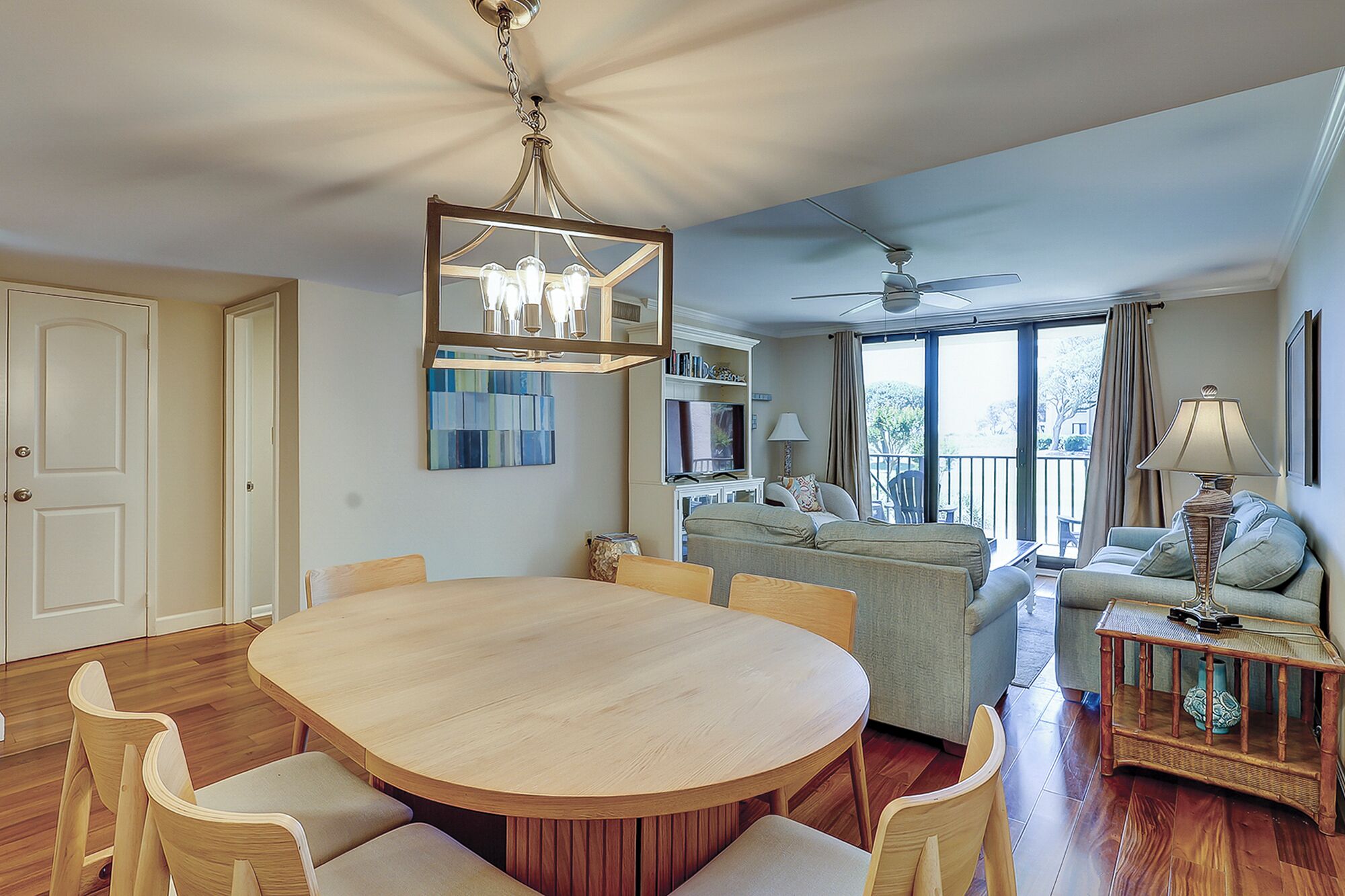 A dining area with a round table and chairs, a ceiling fan, and a view through a large window.