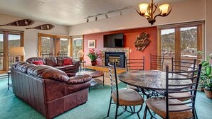 A spacious living room with a fireplace, leather sofa, dining table, and chairs. - Village Penthouse At Wetterhorn Condo: Ski-In/Out (Breckenridge)