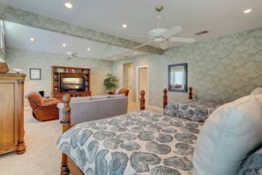A bedroom with a large bed, a TV, a bookshelf, and a ceiling fan.