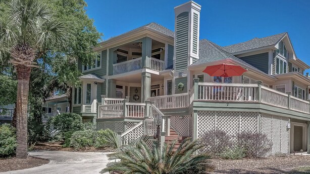 Une maison à deux étages avec un balcon, une véranda et un parasol rouge.