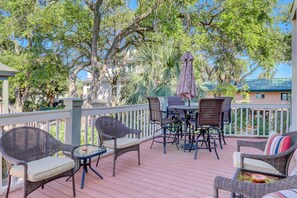 An outdoor deck with wicker furniture, a glass table, and a patterned umbrella.