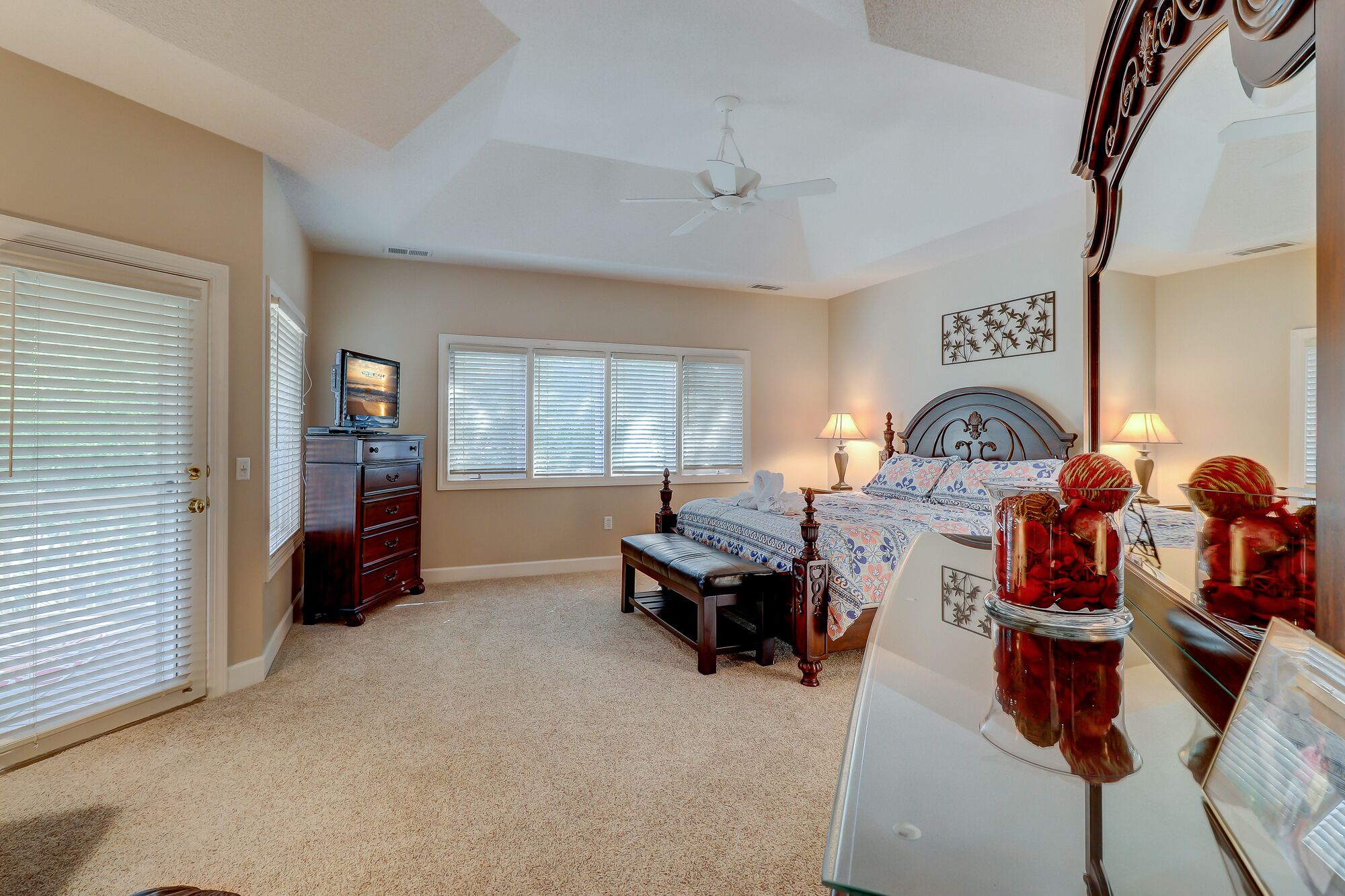 A bedroom with a bed, a dresser, a bench, a ceiling fan, and a window with blinds.