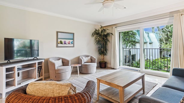 A living room with a television, two armchairs, a coffee table, and a large window with a view of greenery.