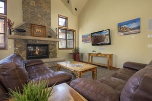Una sala de estar acogedora con sofás de cuero, una chimenea de piedra, un televisor y obras de arte en las paredes.