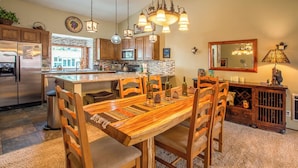 Una cocina con una isla central, mesa de comedor de madera, sillas y un candelabro.