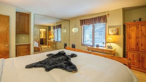 Un dormitorio con una cama grande, un armario de madera, un espejo y una ventana con persianas.