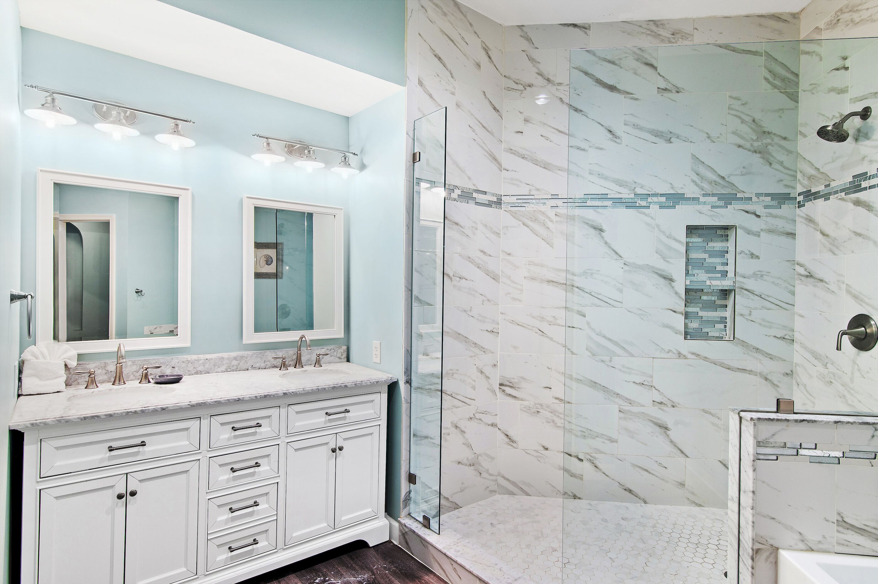 A bathroom with a marble shower, a double sink vanity, and a glass-enclosed shower area.