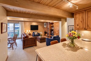 A spacious living area with a fireplace, wooden furniture, and a view through a large window. - Top Floor Condo w/ Mountain Views & Charm (Aspen)