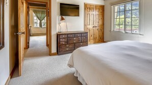 Une chambre à coucher avec un grand lit, une commode, un téléviseur fixé au mur et une fenêtre donnant sur l’extérieur.
