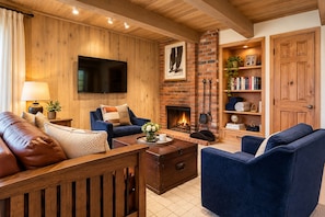 A cozy living room with a fireplace, wooden walls, a flat-screen TV, and a bookshelf. - Top Floor Condo w/ Mountain Views & Charm (Aspen)