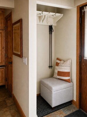 A corner with a grey cushioned bench, a black floor mat, a white ceiling-mounted light fixture, and a wooden door.